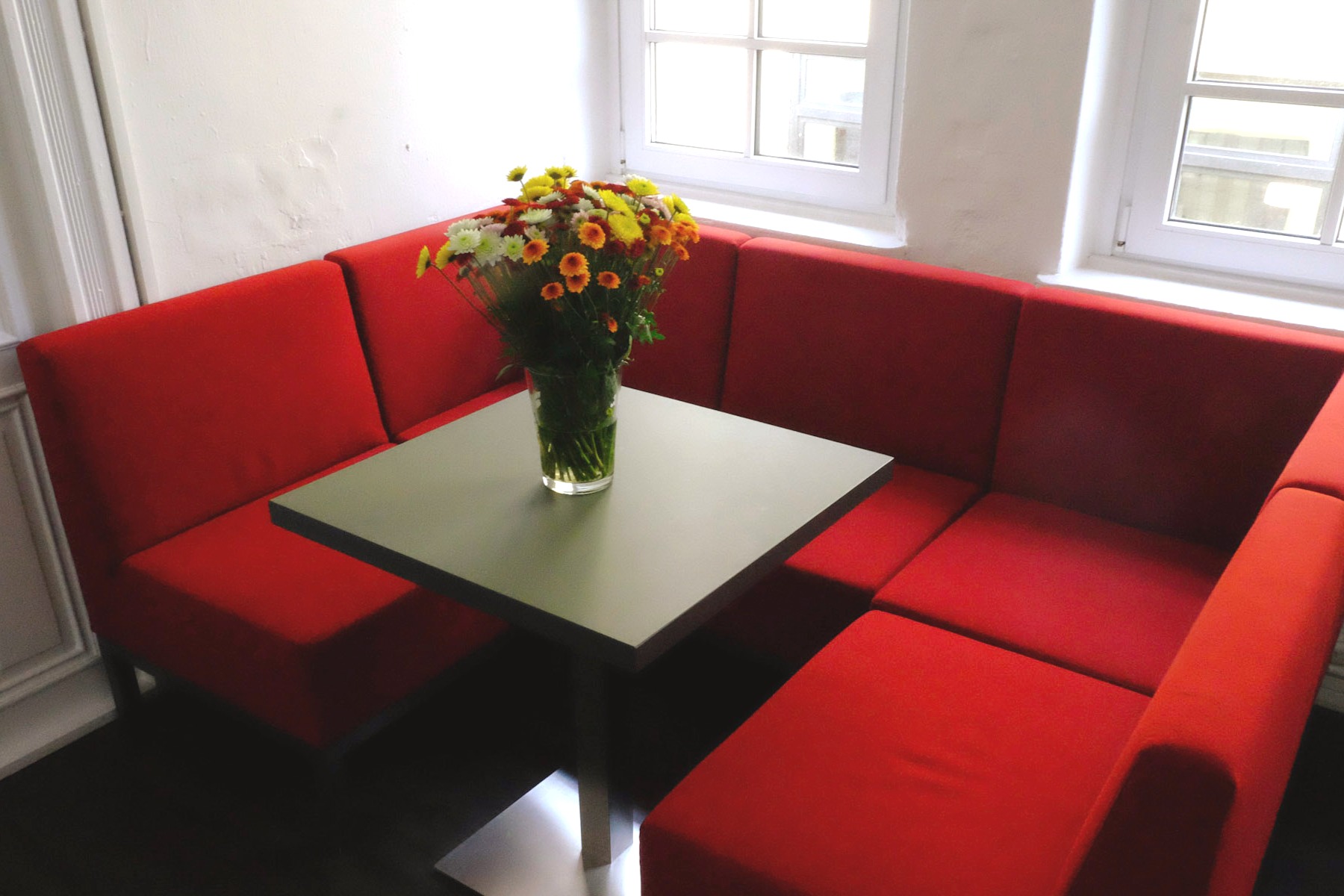 Rote Polstersitzecke mit grünem Tisch und sommerlichem Blumenstrauß